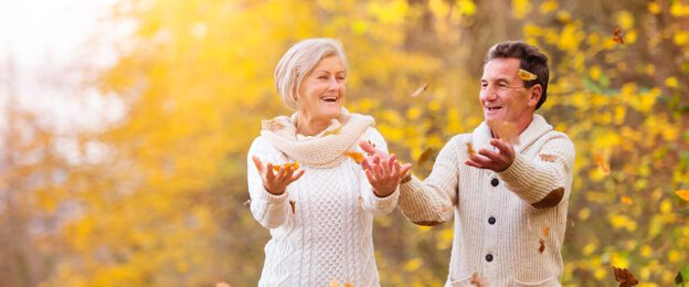 Senior couple tossing leaves in autumn park