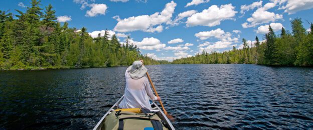 Person paddling canoe on forested lake